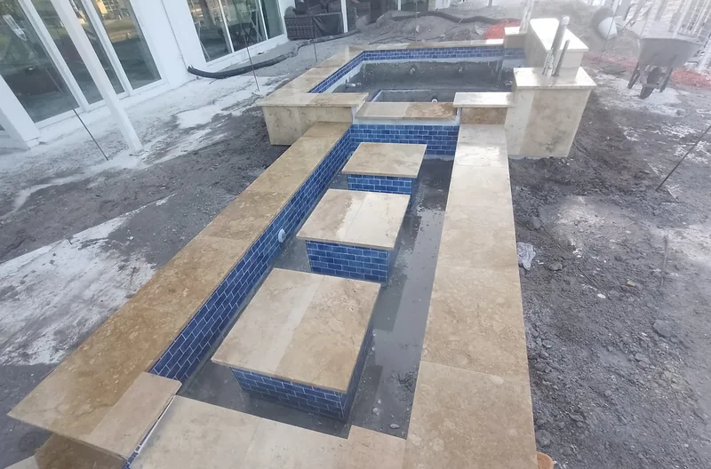 Travertine stepping stones across blue tile channels beside a pool