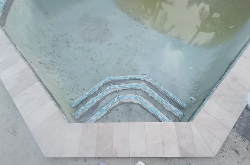 Looking down on pool steps trimmed with blue tile and a travertine edge